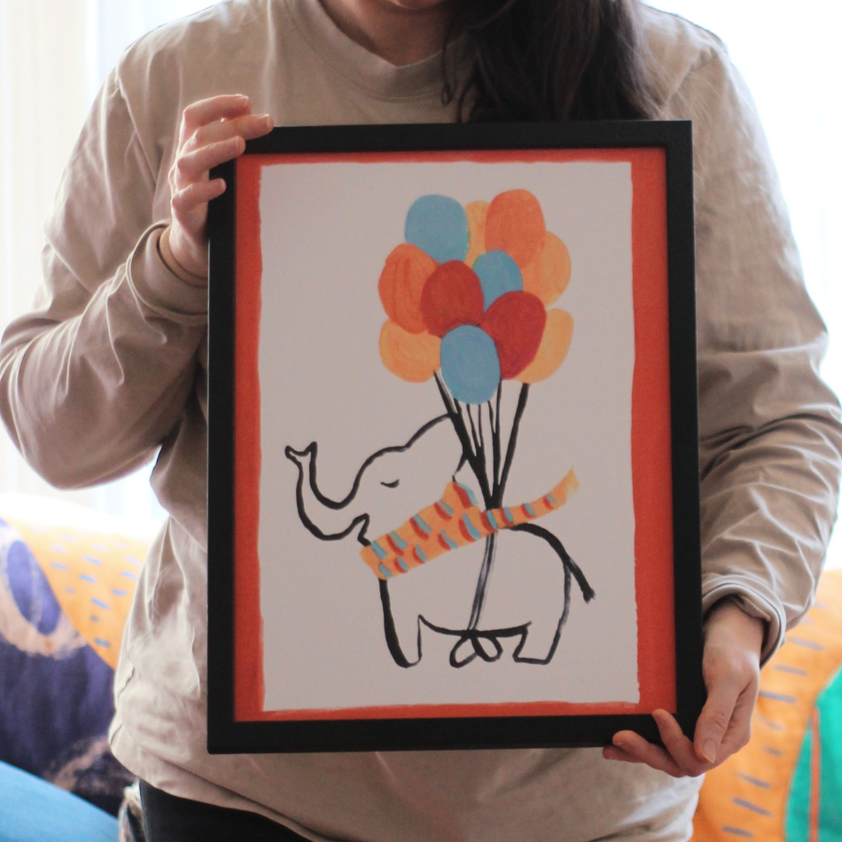 Person holding a framed drawing of an elephant with balloons.