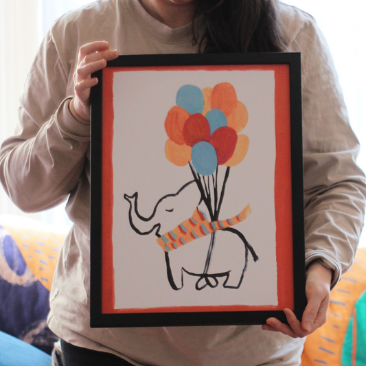 Person holding a framed drawing of an elephant with balloons.